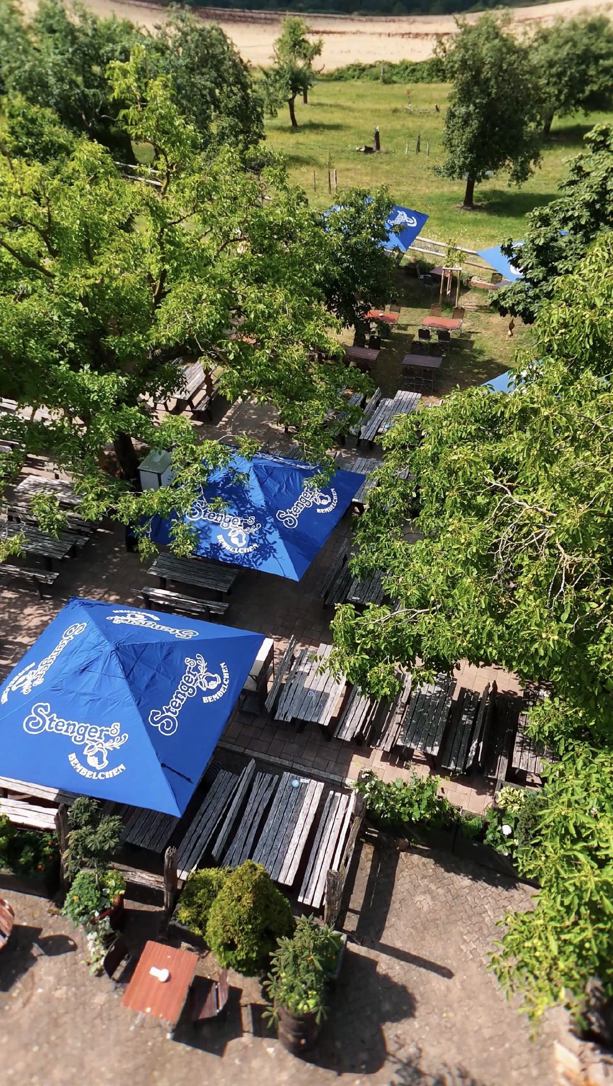 Blick von oben auf den Bembelgarten mit den blauen Stenger-Schirmen zwischen den Bäumen